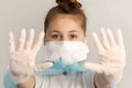 Close-up teenager girl in surgical protective mask and rubber gloves on a neutral gray background.