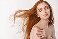 Close-up of tender young woman with long natural red hair flying in air, close eyes and relaxing on white background Royalty Free Stock Photo