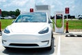 Close-up Tesla Model 3 charging at Tesla Supercharger Station in large gas station parking lot hot summer day
