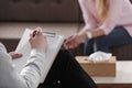 Close-up of therapist hand writing notes during a counseling session with a single woman sitting on a couch in the blurred Royalty Free Stock Photo
