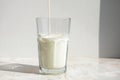 Close-up of thin stream of fresh milk pouring into glass standing on a light table