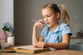 Close-up of thinking pretty elementary child school girl doing homework and holding pen against mouth sitting at home Royalty Free Stock Photo