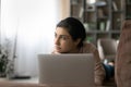 Close up thoughtful Indian woman lying on couch with laptop