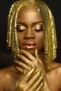 Close-up of thoughtful young black woman with closed eyes and golden accessories, make-up holding hands under the chin Royalty Free Stock Photo