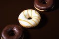 Close-up three glazed donuts are lying on diagonal on dark chocolate background.