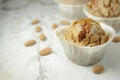 Close-up of three muffins on a wooden table with a white tablecloth and several almonds.