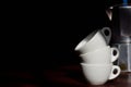 Close-up of three old white espresso cups stacked on top of each other in front of a vintage Italian coffee maker made in Italy,