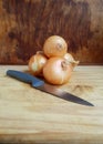 Three onions arranged on a chopping board with a knife Royalty Free Stock Photo