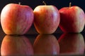 Close-up of three red apples on dark glass. black background