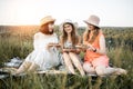 Pretty women, sitting on the blanket on picnic, holding wooden round plates with escargot snails