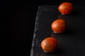 Close-up of three wet kumato cherry tomatoes, with selective focus, on black slate and black background horizontally Royalty Free Stock Photo