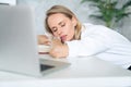 Close up of a tired businesswoman wearing white clothes and sleeping near her laptop in an office with white and green binders Royalty Free Stock Photo