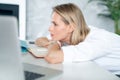 Close up of a tired businesswoman wearing white clothes and thinking near her laptop in an office with white and green binders Royalty Free Stock Photo