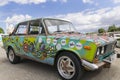 Close Up to a Green Lada car painted in hippie style with cloudy blue at background