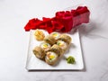 Close up to hot tempura sushi roll with salmon. Red rose petals near served dish on marble background. Breaded Sushi roll portion