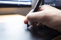 Close up to a male hand holding up a black digital pencil over a black and green drawing tablet in desk and home office background Royalty Free Stock Photo