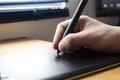 Close up to a male hand holding up a black digital pencil over a black and green drawing tablet in desk and home office background Royalty Free Stock Photo