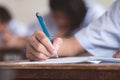 Close-up to student holding pen and writing final exam in examination room or study in classroom