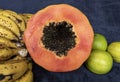 Close up to a top view of a fresh sliced orange papaya with seeds inside, a freckled bananas cluster and three green lemons over a Royalty Free Stock Photo