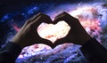 Close up to a two male hands making sign heart by fingers to a beautiful colorful circular galaxy at background