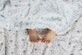 Close-up of toddler girl`s feet on the bed under the blanket. Light blue and beige tones Royalty Free Stock Photo