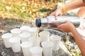 Close-up top above view woman hand hold steel thermos pouring hot tea many white paper cup group picnic mountain