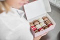 Close up top angle view of colorful macarons in a gift box in hands of female confectioner. Traditional french dessert