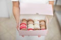 Close up top angle view of colorful macarons in a gift box in hands of female confectioner. Traditional french dessert