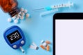 Close up top down view of glucose meter, drug pills, insulin syringe and tablet pc with blank white screen for copy space on blue