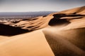 Close up of the top of a sand dune with sand particles being blown over the top. Desert landscape with wind