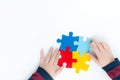 Close up and top view of autistic child`s hands holding and arranging colorful jigsaw puzzle on white table top background. Royalty Free Stock Photo