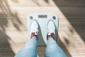 Close up and top view of creative casual dressed feet on scales asking for help. Lose weight and measuring concept. Wooden floor