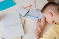 Close up top view of exhausted pupil boy sitting at home or classroom lying on desk filled with books training material Royalty Free Stock Photo