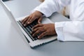 Close-up top view hands of unrecognizable African-American practitioner male doctor wearing white coat working typing on Royalty Free Stock Photo