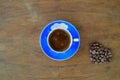 Close-up and top view of hot black coffee in blue coffee cup and roasted Thai coffee beans on wooden background. Royalty Free Stock Photo