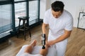 Close-up top view of professional male masseur massaging leg calf muscles using massage gun percussion tool of muscular Royalty Free Stock Photo