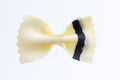Close up top view shot of an isolated white and black colored raw Italian farfalle bow pasta on a white background