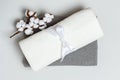 Close-up top view of a stack of rolled up white and gray towels with a cotton branch