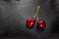 Close-up top view of two heart-shaped red cherries on black textured background with copy-space