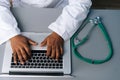 Close-up top view of unrecognizable African practitioner male doctor in white coat uniform working typing on laptop