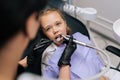 Close-up top view of unrecognizable female orthodontist examining teeth of cute little child girl with dental equipment