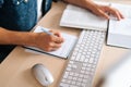 Close-up top view of unrecognizable male student studying online from home using computer, writing notes, watching video