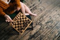 Close-up top view of unrecognizable woman making chess move sitting on armchair in dark room with vintage wooden floor. Royalty Free Stock Photo