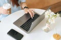 Close-up top view of unrecognizable young woman sitting at desk with laptop and holding in hands cup with hot coffee at