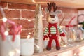 Close up toy amigurumi deer in striped sweater and stylish red butterfly tie stands on the wooden shelf near the