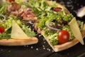Close up of pizza slice near uncut pizza with jamon, Parmesan cheese, black olives and cherry tomatoes Royalty Free Stock Photo