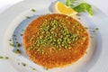 Traditional turkish kunefe dessert with grated pistachios, sliced lemon and mint on plate.