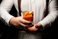 Close-up of transparent glass with cold alcoholic cocktail with orange zest in male hand Royalty Free Stock Photo