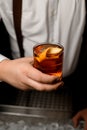 Close-up of transparent glass with cold alcoholic drink with orange zest in male hand Royalty Free Stock Photo