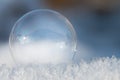 Close-up of a transparent and glowing soap bubble lying on glittering snow. The soap bubble looks like a glass ball. The Royalty Free Stock Photo